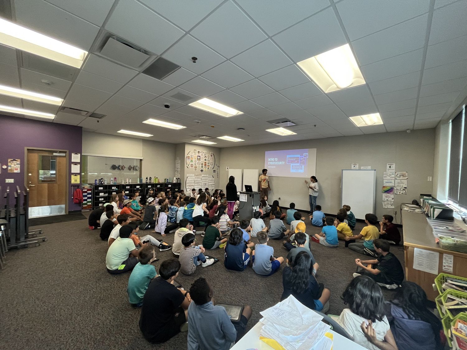 Elementary students seated on the floor watching a CyberCEO presentation